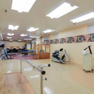 A spacious rehabilitation therapy room equipped with various exercise machines and parallel bars.