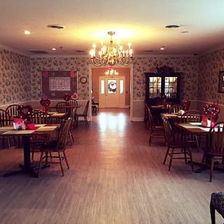 A warmly lit dining area with elegantly arranged tables and chairs, featuring a chandelier.