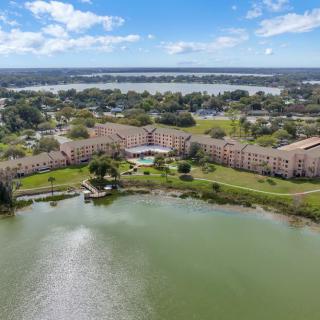 Aerial view of an apartment complex situated by a lake, with a cloudy sky in the background.