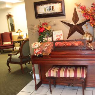 A cozy living room with a decorative piano and floral arrangements.