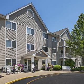 A residential apartment building with light-colored siding and a well-maintained entrance surrounded by greenery.
