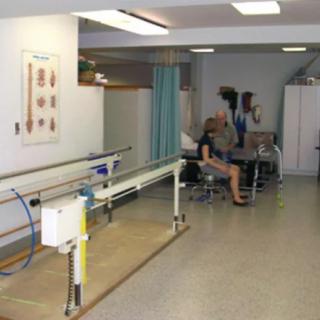 A physical therapy room with parallel bars and a therapist assisting a patient.