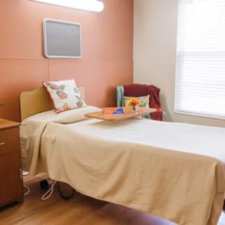 A hospital room with a bed, nightstand, and chair by the window.