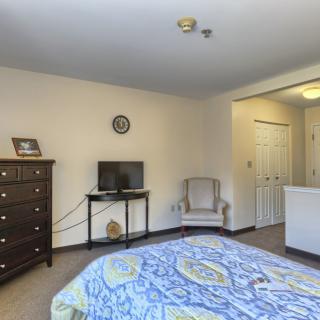 A spacious bedroom with a bed, dresser, TV, and chair.