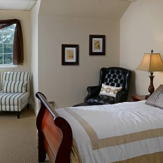 A cozy bedroom with a wooden bed, armchair, and window.