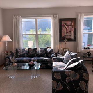 A cozy living room with a patterned sofa and armchair, complemented by a glass coffee table, floor lamp, and large windows with curtains.