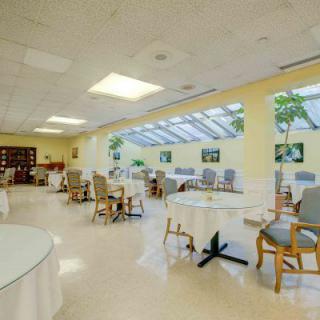 A spacious dining area with large windows allowing natural light to brighten the room, featuring arranged tables and chairs.