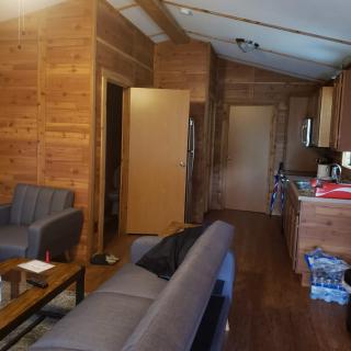 A cozy living area with wood paneling, featuring a sofa, chairs, and an adjoining kitchen.