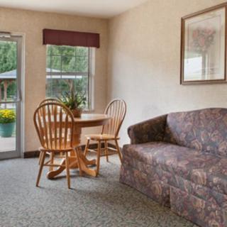 A cozy living room with a round wooden table, two chairs, and a patterned sofa near a window.