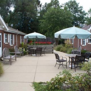A cozy outdoor patio area with umbrellas and seating surrounded by brick buildings and greenery.