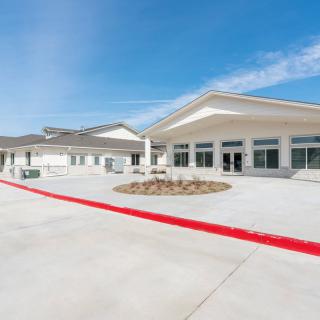 A modern commercial building with a spacious concrete driveway and clear blue sky.