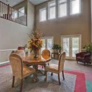 A well-lit living room featuring a round table with elegant chairs, large windows, and decorative elements.