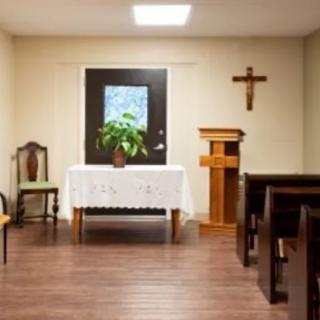 A small chapel interior with an altar, seating, and a cross on the wall.