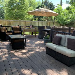 A sunny outdoor deck with comfortable patio furniture and an umbrella.