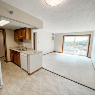 A bright apartment with an open floor plan, featuring a kitchen and living area with sliding doors leading to a balcony.