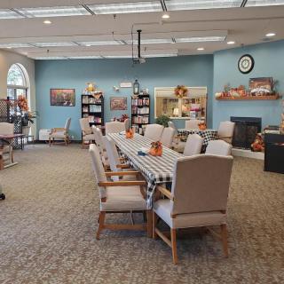 A cozy dining area with a long table and comfortable chairs, surrounded by bookshelves and decorative elements.