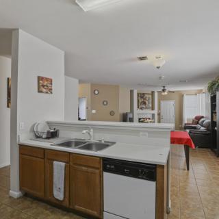 A cozy kitchen with wooden cabinets and a marble countertop, opening into a spacious living area.