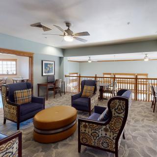 A cozy living room with comfortable seating arrangements, featuring patterned armchairs and a central ottoman beneath ceiling fans.
