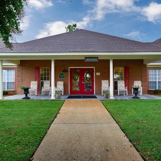 A welcoming house with a red door, white porch columns, and a green lawn under a cloudy sky.