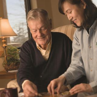 An elderly man and a caregiver engaging in a shared activity indoors.
