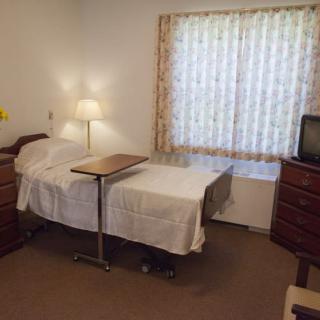 A room with a hospital bed, side lamp, and television.