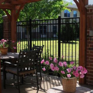 A cozy patio with a pergola, adorned with flowers and outdoor furniture, overlooking a fenced garden.