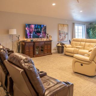 A cozy living room featuring recliner chairs and a sofa, with a large TV for home theater enjoyment.