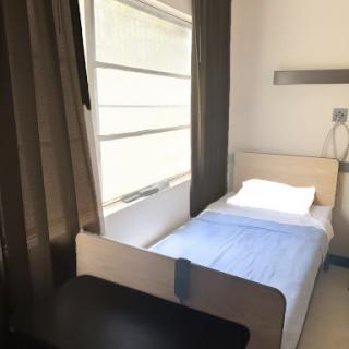 A clean and minimalist hospital room featuring a single bed and natural light from the window.