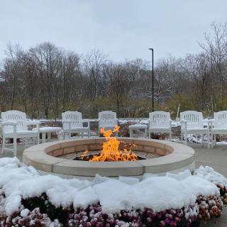 A cozy fire pit surrounded by snow-covered chairs on a chilly winter day.
