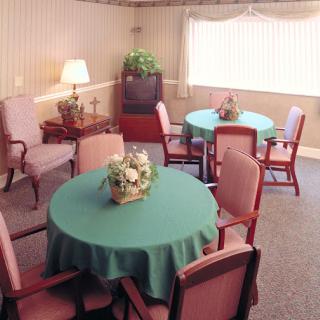 A cozy seating area featuring round tables with green tablecloths and comfortable chairs.