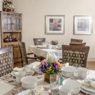 A neatly set dining room table with dishware and a flower centerpiece, surrounded by wooden chairs and decorated walls.