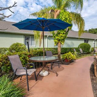A serene patio area with a table, chairs, and an umbrella next to a garden pathway.
