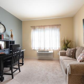 A cozy living room with a sofa, desk, and window letting in natural light.