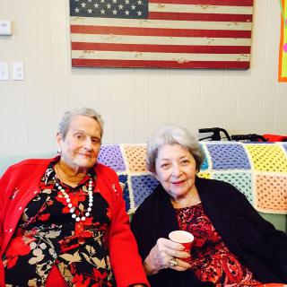 Two elderly women sitting together with an American flag in the background.