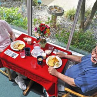Two people enjoying a meal at a table with a red tablecloth next to large windows.