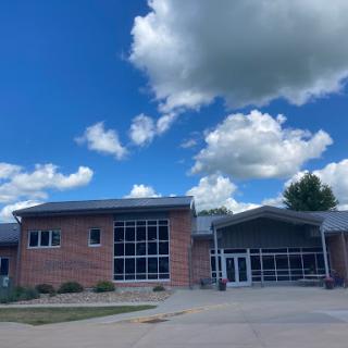 A modern brick building under a clear blue sky adorned with fluffy clouds.