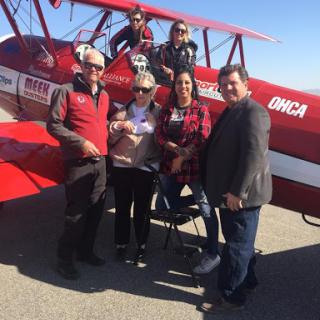 A group of people gathered in front of a red biplane, enjoying a moment together.