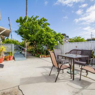 A sunny backyard patio with outdoor seating and lush green plants.