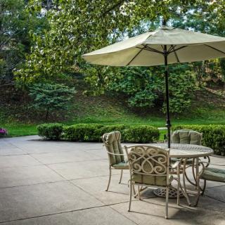 A peaceful outdoor patio with a table and chairs under an umbrella surrounded by lush greenery.