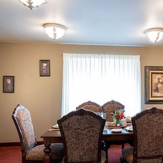 A cozy dining room featuring a wooden table set with patterned chairs, illuminated by ceiling lights and adorned with wall art.