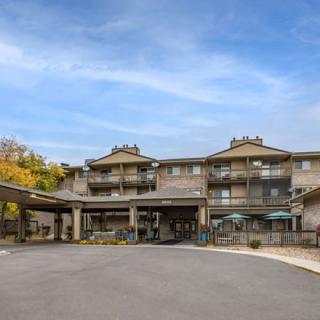 A front view of a hotel building with multiple stories, featuring a covered entrance and surrounded by trees under a partly cloudy sky.