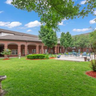 A scenic view of a building courtyard with lush green lawn, trees, and patio area.