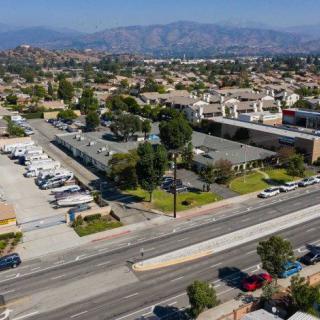 Aerial view of a suburban area with roads, buildings, and vehicles parked in lots, set against a backdrop of distant mountains.