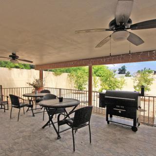 A spacious patio with ceiling fans, outdoor seating, and a grill in a backyard setting.