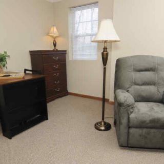 A cozy living room corner with an armchair, floor lamp, and dresser by the window.