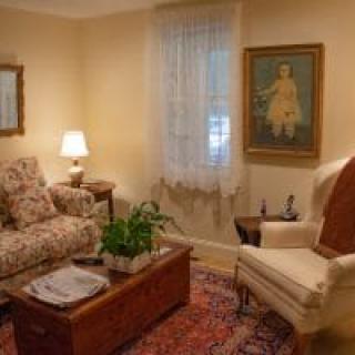 A cozy living room with a patterned sofa, armchair, and coffee table, adorned with a rug and artwork on the wall.