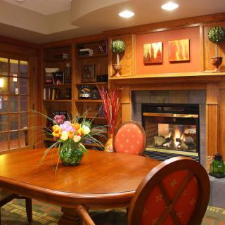 A cozy dining room with wooden furniture and a fireplace, adorned with bookshelves and floral decor.