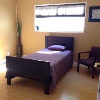 A minimalist bedroom with a single bed featuring purple bedding, wooden furniture, and natural lighting.