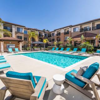 A sunny outdoor swimming pool area with lounge chairs at an apartment complex.