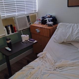 A cozy bedroom with an unmade bed and a nightstand filled with personal items.